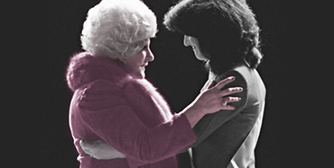 Mary Kay Ash fica em frente a uma consultora da Força de Vendas Independente em uma conversa com suas mãos nos ombros da mulher.
